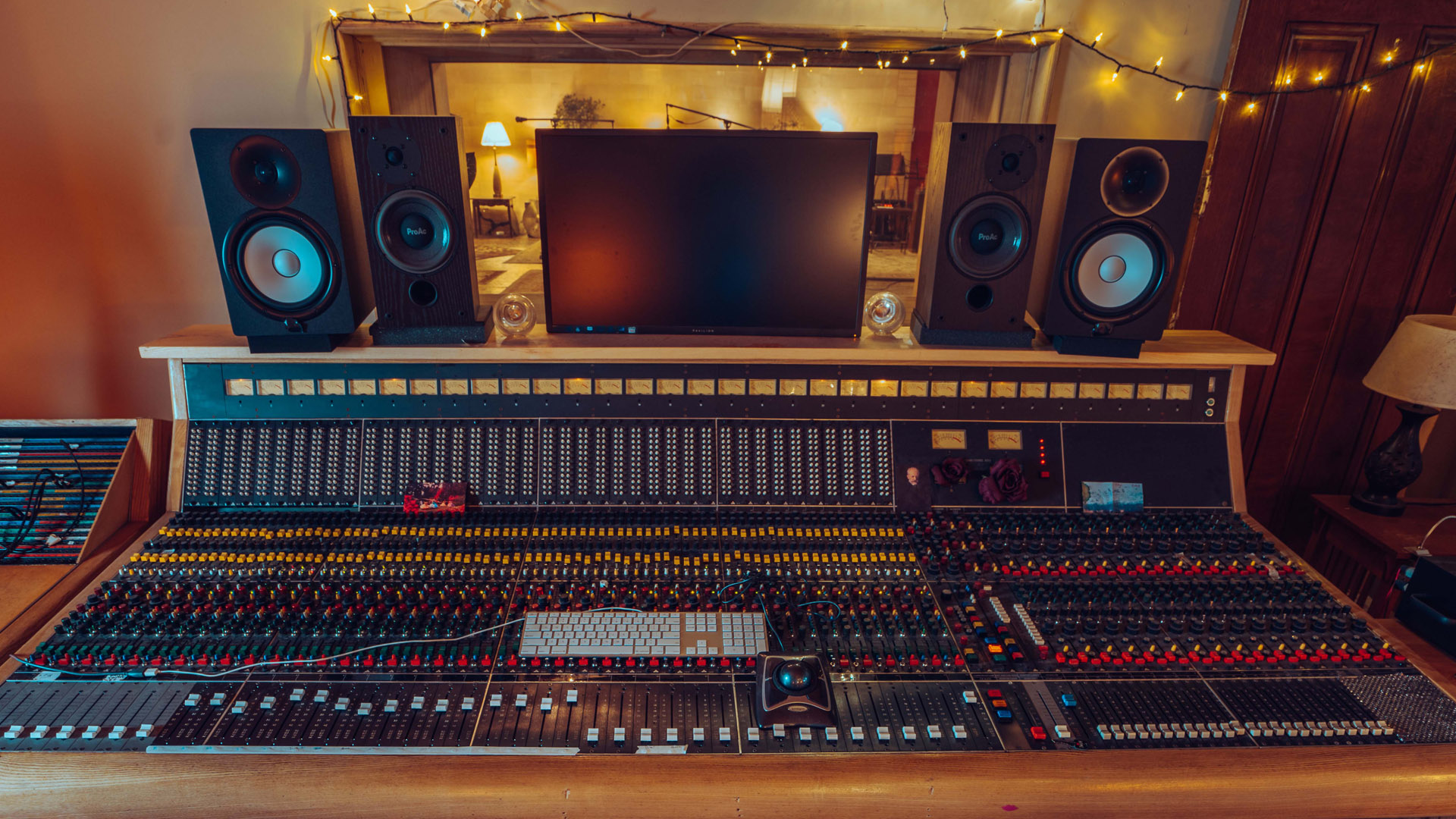 Large digital mixing board within a sound room looking out into the live room.