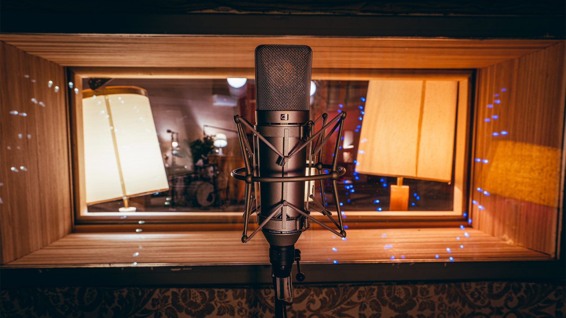 Large image from within a whisper room looking out into the studio, with a microphone front and center.