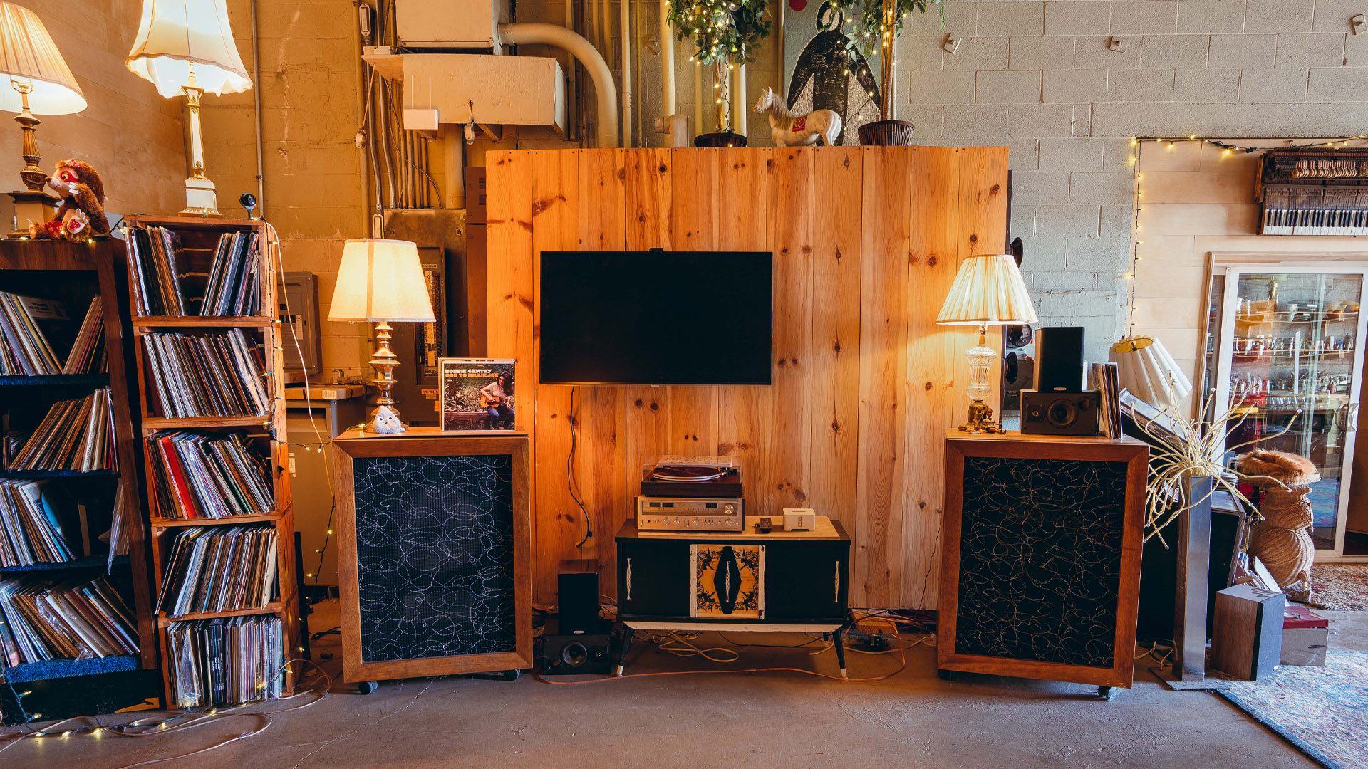 Wooden wall with mounted TV, floor speakers and records surrounding, and a record player under.