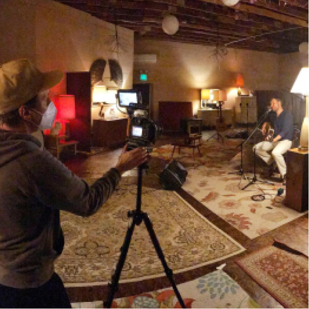 Still from a video shoot featuring a cinematographer recording a person playing guitar and singing.