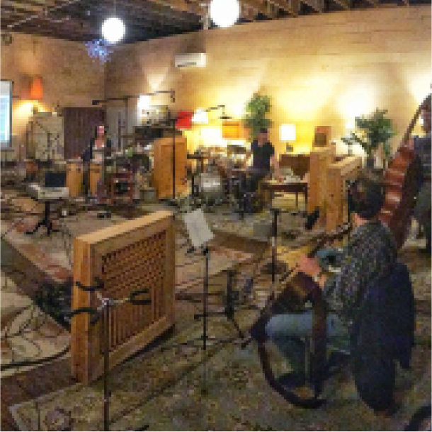 Multiple people playing instruments together in large studio room.